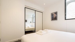 Une chambre d’hôtel moderne dotée d’un grand lit, d’un placard à portes coulissantes, d’un tableau encadré au mur et d’une fenêtre laissant entrer la lumière naturelle.