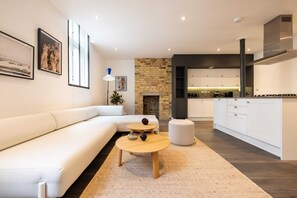 Een moderne woonkamer met een witte bank, een ronde houten salontafel en een open haard.