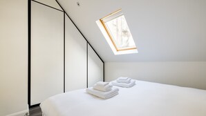 Ein modernes Schlafzimmer mit Dachfenster, einem ordentlich bezogenen Bett und einem minimalistischen Design.