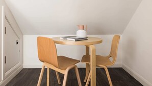 Ein kleiner, runder Holztisch mit zwei passenden Stühlen, einer weißen Vase und einem Buch mit dem Titel „CHANEL“.