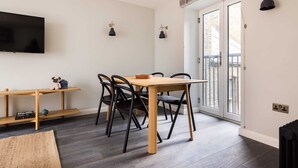 Ein modernes Wohnzimmer mit einem Holzesstisch, schwarzen Stühlen, einem flachbildfernseher an der Wand und einer Glasschiebetür, die zu einem Außenbereich führt.