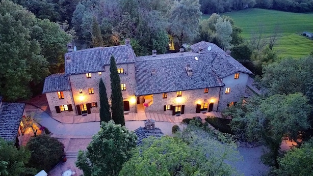 A large stone building with multiple windows and a central staircase, surrounded by trees and a green field. - HAMLET THE POET - HOUSE SANTA LUCIA (Umbria)