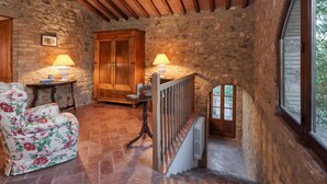A rustic interior with stone walls, wooden beams, a staircase, and a floral armchair. - HAMLET THE POET - HOUSE SANTA LUCIA (Umbria)
