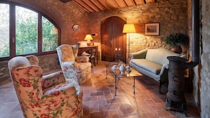 A cozy room with stone walls, wooden beams, a fireplace, floral armchairs, and a sofa. - HAMLET THE POET - HOUSE SANTA LUCIA (Umbria)