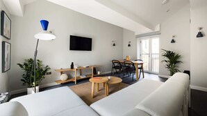 A modern living room with a sofa, a coffee table, a TV, and a dining area with chairs and a table. - Marvellous Leicester Sq 2BR - Netflix & Nespresso (London)