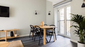 A modern living room with a wooden dining table, black chairs, a flat-screen TV mounted on the wall, and a large potted plant. - Marvellous Leicester Sq 2BR - Netflix & Nespresso (London)