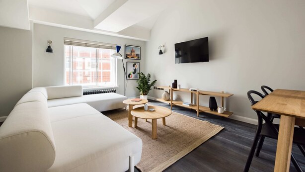 A modern living room with a white sofa, a wooden dining table, and a TV mounted on the wall. - Marvellous Leicester Sq 2BR - Netflix & Nespresso (London)