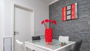 A modern dining area with a glass-top table, white chairs, and a red vase with flowers. - Modern villa, shared infinity pool | SunsetCliff 4 (Faja Da Ovelha)