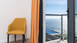 A yellow chair next to a sliding glass door with a view of a pool and the sea. - Modern villa, shared infinity pool | SunsetCliff 4 (Faja Da Ovelha)