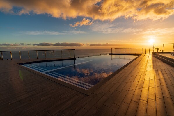 A swimming pool with a wooden deck and a view of the sea at sunset.