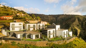 A modern residential complex with multiple two-story houses, featuring balconies, large windows, and a stone retaining wall. - Modern villa, shared infinity pool | SunsetCliff 7 (Faja Da Ovelha)