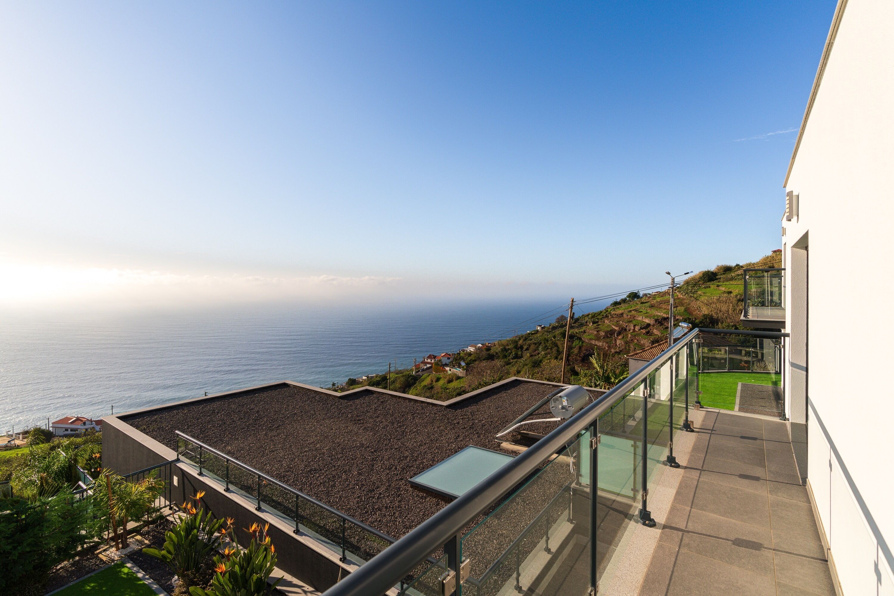 Eine Dachterrasse mit Blick auf das Meer, einer Glasuhrung und einem gepflasterten Weg.