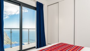Une chambre d’hôtel avec une grande fenêtre, un lit recouvert d’une courtepointe à rayures et une vue sur l’océan.