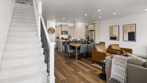 Una cocina moderna con armarios blancos, un comedor con sillas grises y una escalera con escalones blancos.