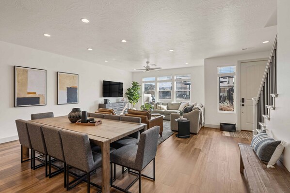 A spacious living area with a wooden dining table, comfortable seating, and a large window providing a view of the outside.