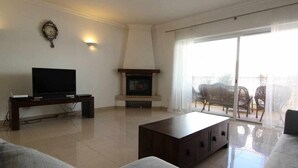 Una sala de estar con televisor de pantalla plana, chimenea, sofá y balcón con mobiliario exterior.