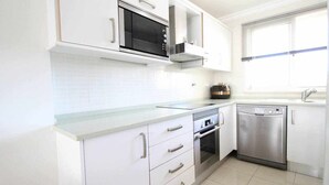 Una cocina moderna con armarios blancos, microondas, horno y lavavajillas.