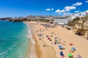 Uma praia com uma fileira de edifícios brancos, céu claro e mar calmo.