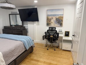 Une chambre à coucher comprenant un lit, un bureau, une chaise, un téléviseur, une commode et un tableau.