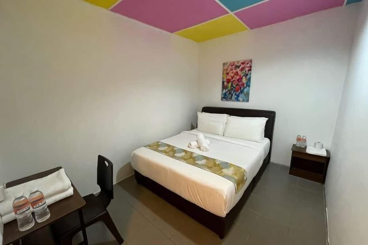 A hotel room with a bed, a small table with a chair, a nightstand, and a colorful ceiling.