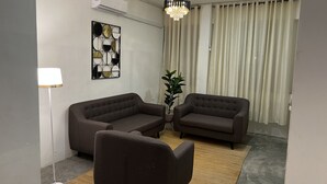 Un saló modern amb dos sofàs, una làmpada de peu, una obra decorativa a la paret i una finestra gran amb cortines.