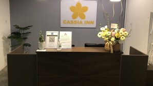 Taulell de recepció a Cassia Inn amb un logotip, un codi QR i un arranjament floral.