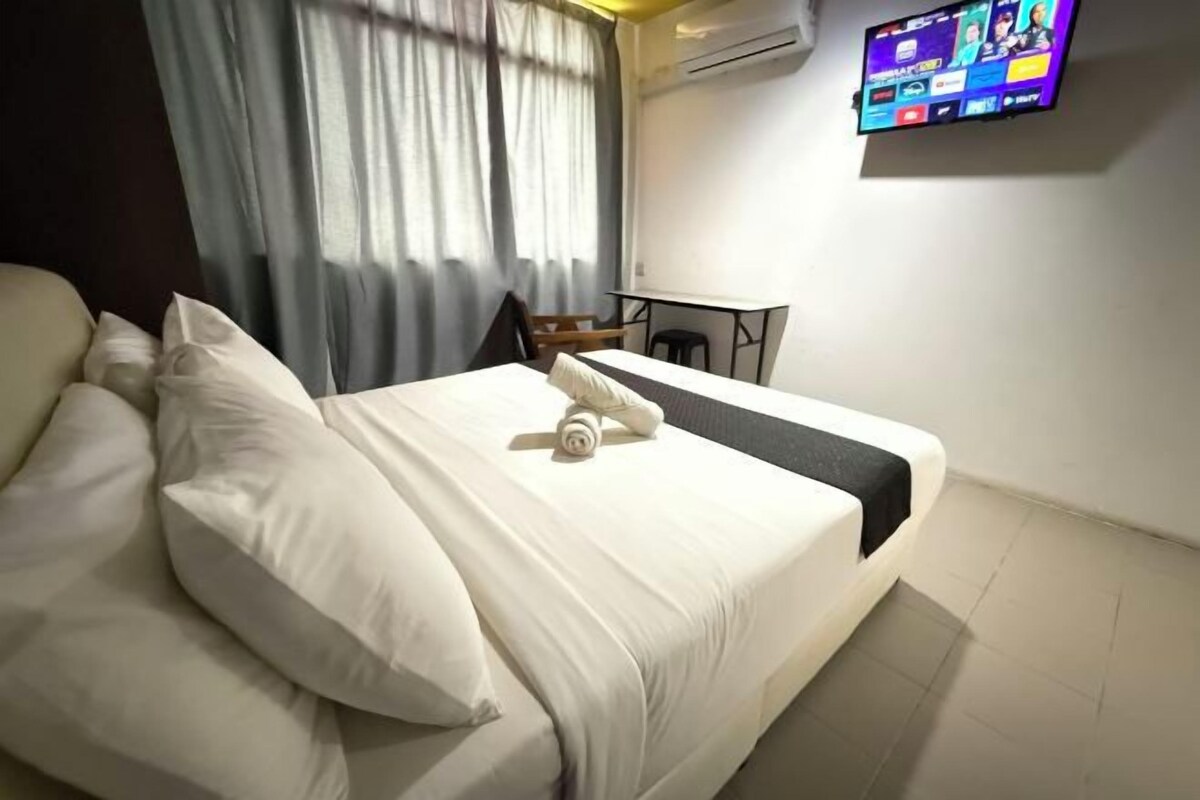 Een hotelkamer met een bed, kussens, een bureau en een flatscreen televisie aan de muur.