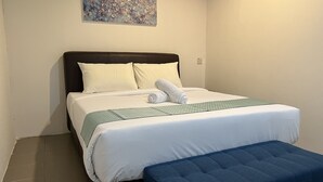 Un llit ben arropat amb roba de llit blanca i verda, un banc blau al peu del llit i un quadre penjat a la paret de sobre.