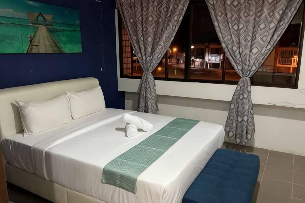 A neatly made bed with a pillow, a green bedspread, and a blue bench.