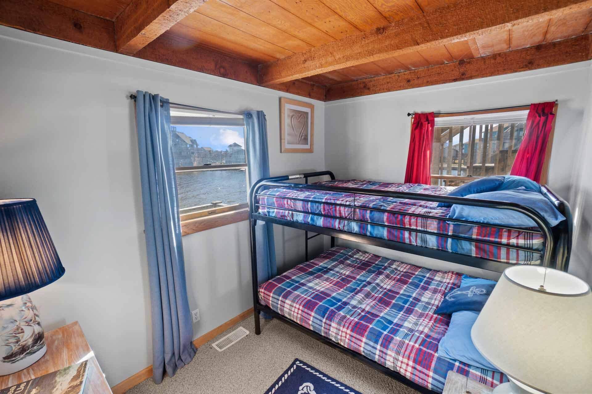 Una pequeña habitación tipo cabaña con literas, una ventana con vistas a un cuerpo de agua y una lámpara sobre una mesita.