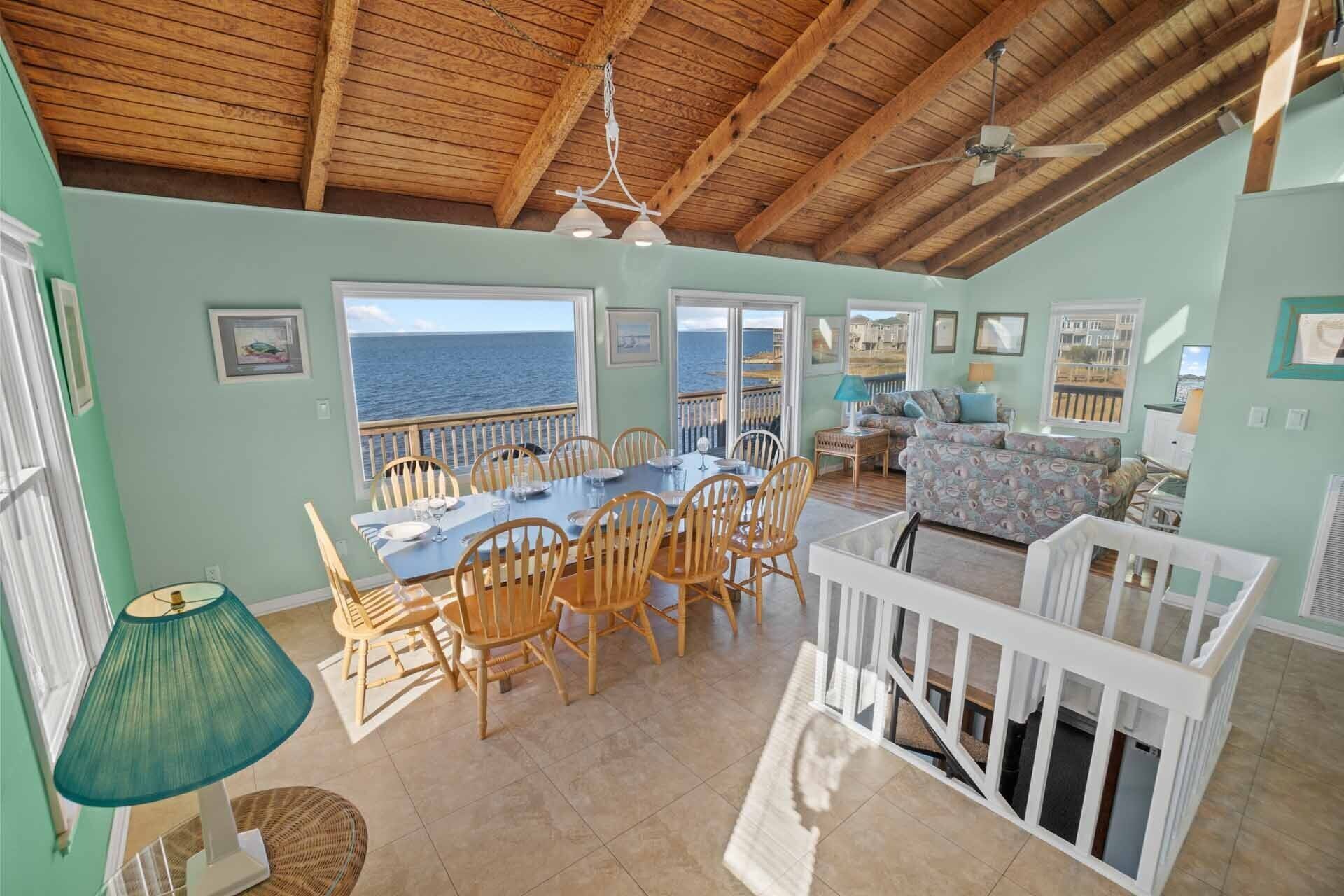 A spacious dining area with a view of the sea, wooden furniture, and a ceiling fan.