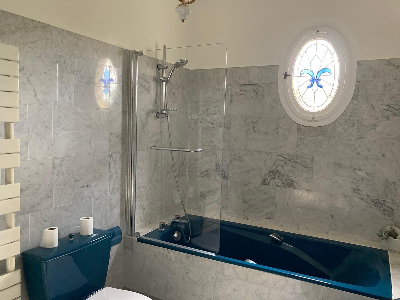 A modern bathroom with a glass-enclosed shower, a blue bathtub, and a toilet.