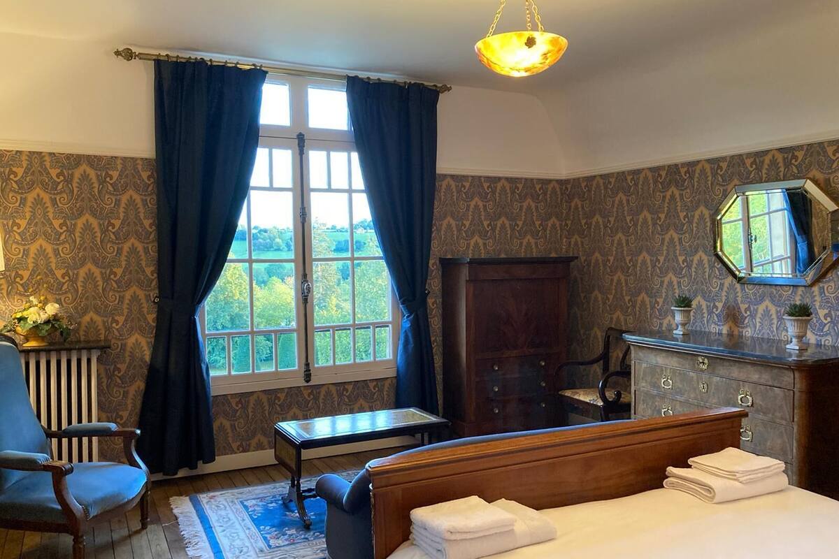 Een slaapkamer met een groot bed, een houten dressoir, een stoel, een bureau en een raam met gordijnen.