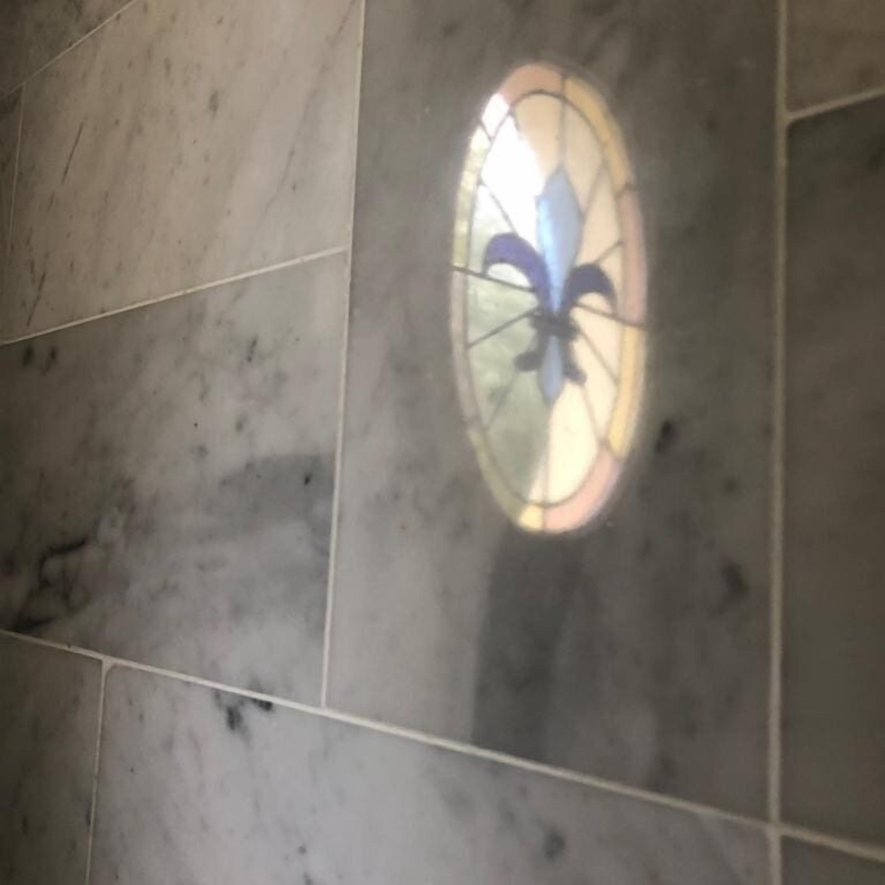 A stained glass window with a fleur-de-lis design on a tiled wall.