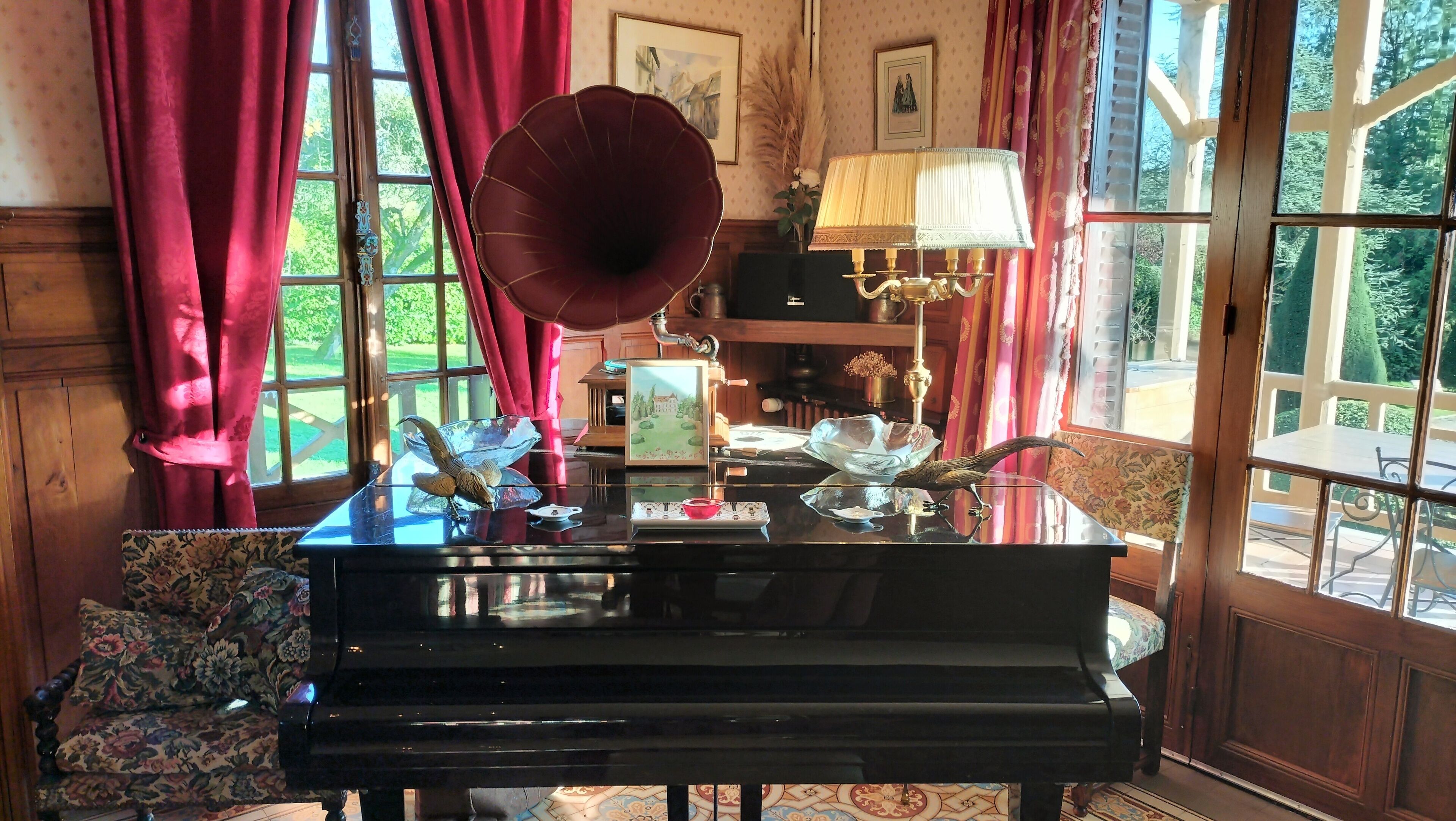A grand piano in a room with large windows, red curtains, and a lamp.
