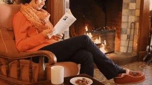 Eine Person sitzt in einem Ledersessel und liest eine Zeitung in einem Raum mit Kamin.