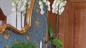 Un mueble de madera con un espejo, un jarrón con orquídeas blancas y un cuenco con plantas verdes.