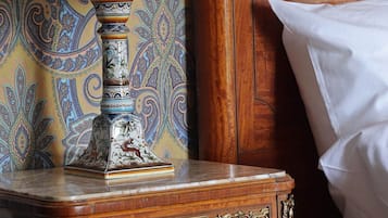 A wooden bedside table with a decorative lamp and a book, against a wall with a paisley-patterned wallpaper.