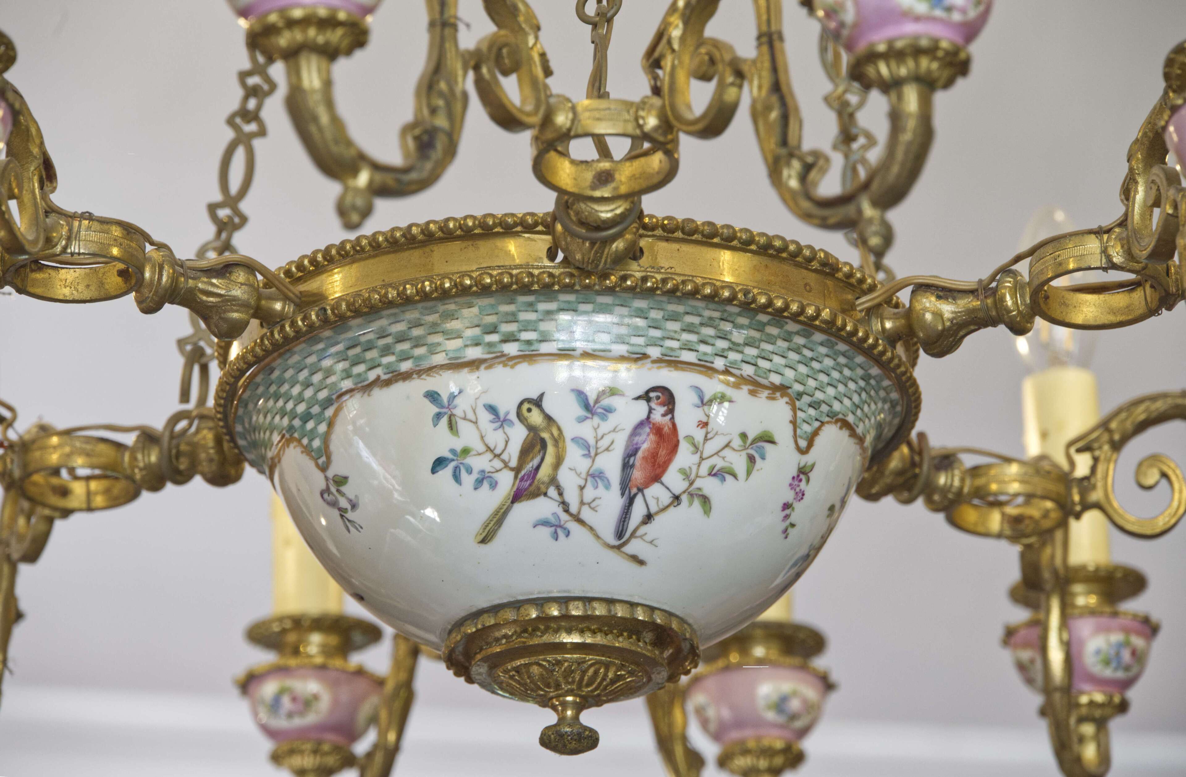 Un candelabro con detalles dorados ornamentados y un recipiente decorativo con aves pintadas.