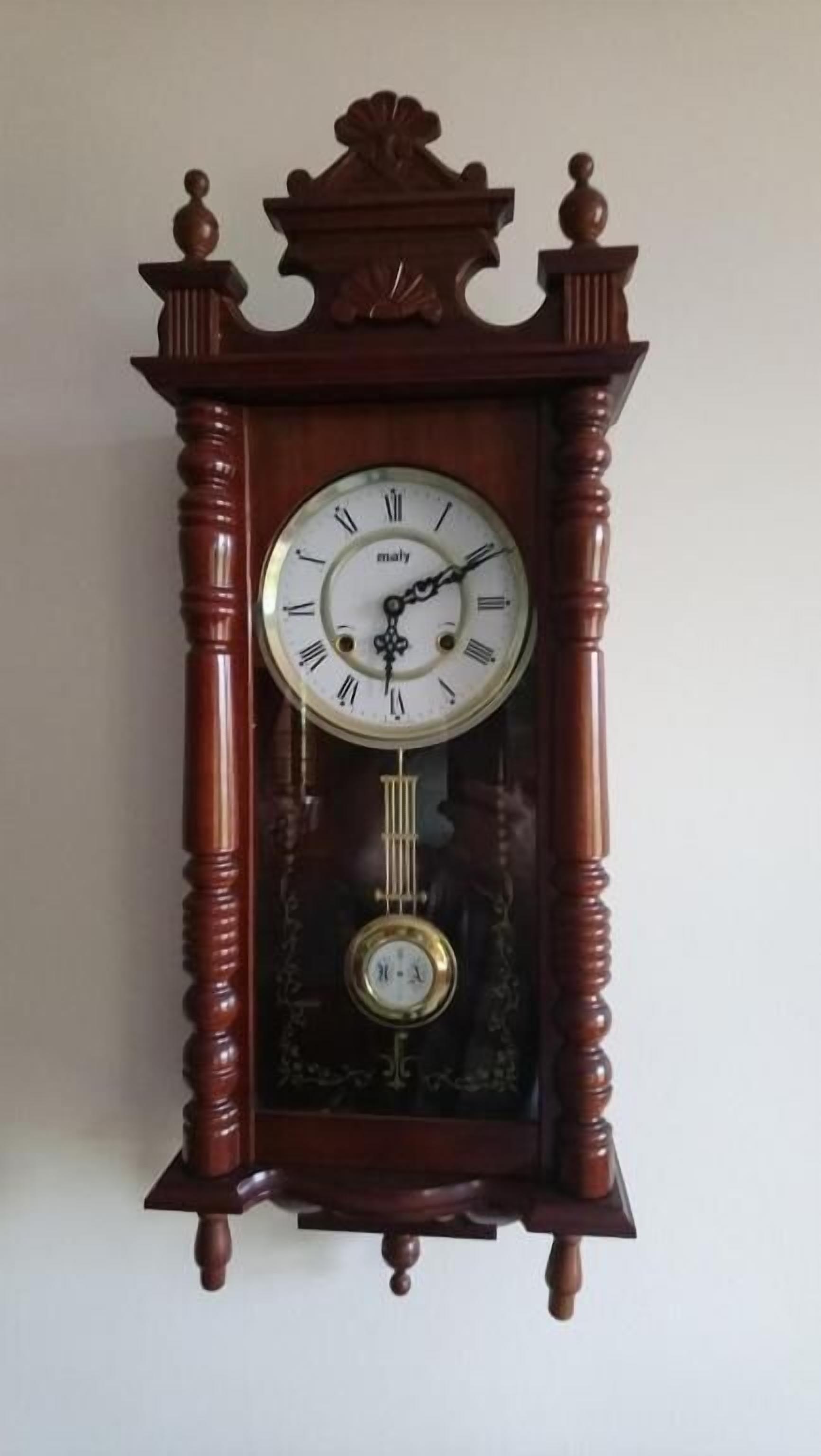 Une grande horloge à coucou en bois, fixée au mur, avec des chiffres romains et un balancier situé sous le cadran.