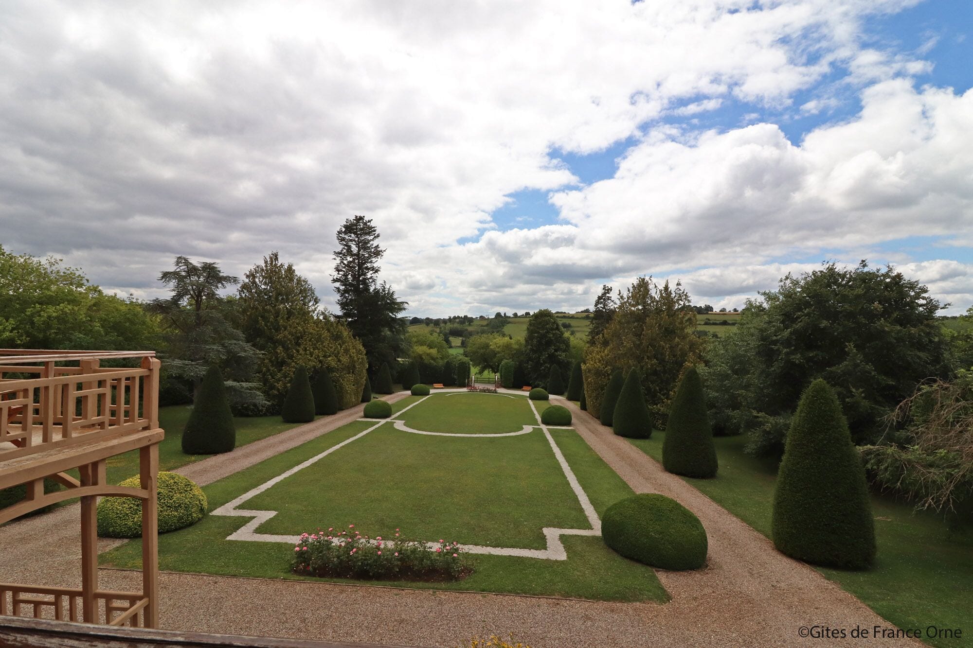A formal garden with neatly trimmed hedges, a central lawn, and a wooden deck.