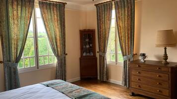 Un dormitorio con cama, cómoda y armario. Hay dos ventanas con cortinas.