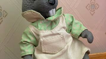 A plush toy rabbit with a green and beige outfit sitting on a wooden surface.