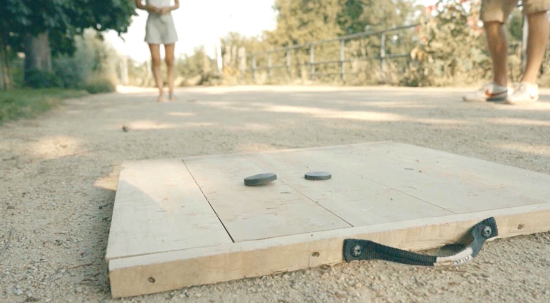 A wooden board game with two metal discs on a gravel surface.