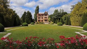 Ein großes, historisches Gebäude mit einem symmetrischen Garten, der ordentlich geschnittene Hecken und einer zentralen Rasenfläche aufweist.