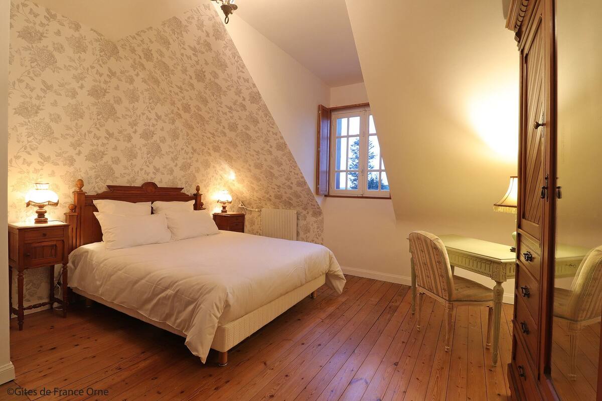 Een slaapkamer met een bed, twee nachtkastjes met lampen, een stoel, een bureau en een dressoir.