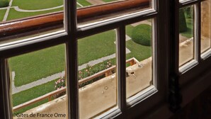 Blick durch ein Fenster auf einen gepflegten Garten und einen bewölkten Himmel.