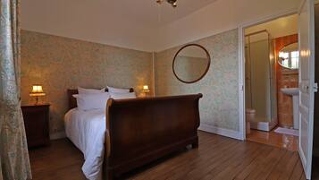 A bedroom with a wooden bed, two bedside lamps, a round mirror, and a bathroom visible through an open door.