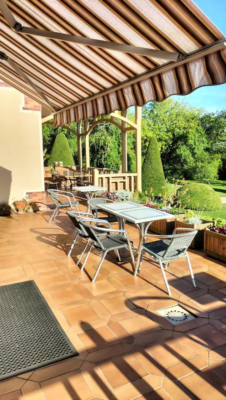 Un patio exterior con suelo de baldosas hexagonales, sillas de metal y una pérgola con toldo a rayas.