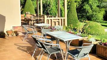 Un patio exterior con suelo de baldosas hexagonales, sillas de metal y una pérgola con toldo a rayas.